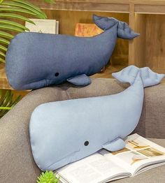 a stuffed whale sitting on top of a couch next to a book and potted plant