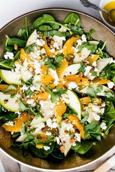 a salad with oranges, spinach and feta cheese in a metal bowl