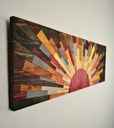 a wooden wall hanging on the side of a white wall with a sun design painted on it