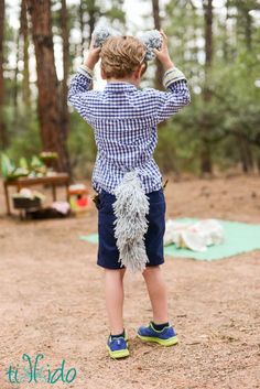 a little boy standing in the woods with his hands on top of his head and looking at something