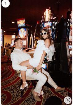 a man and woman dressed in white posing for a photo on the casino floor with slot machines behind them