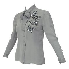 Ethereal and delicate, this blouse is light as a feather but still modest thanks to its perfectly-hued chiffon lining. In true French fashion, the butterflies are embellished with miniature sequins and beads that gently glint without being gaudy. Dove gray long sleeve blouse with banded pussy bow collar, lightly puckered shoulders, turnback cuffs and 4 decorative covered loop buttons at each wrist. Front covered button closure with top and bottom covered snaps and three hand-beaded/sequined blac Black Collared Shirt, Jean Louis Scherrer, Filet Lace, Givenchy Couture, Feather Jacket, Butterfly Blouse, Beaded Blouse, Bow Blouse, Designer Blouses