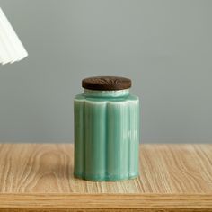 a green jar sitting on top of a wooden table next to a white light bulb