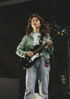 a woman standing in front of a microphone holding a guitar