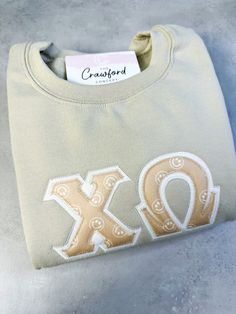 Picture Features1. Chi Omega - Sand Crewneck, White Background Fabric, Sandy Smiles Top Fabric There are 4 parts to your Greek Letter Shirt1. Sweatshirt/Hoodie Color2. Sweatshirt/Hoodie Size3. Background Fabric5. Greek Organization - MAX 3 Greek letters (please contact us for 3+) Add-OnsIf you'd like to add on embroidery on the cuff/sleeve or back, please check the add-on button and detail in the personalization text box what you'd like. Be sure to check spelling! Detail if you'd like a cursive Sorority Letter Sweatshirts, Chi Omega Merch, Sorority Sweatshirt Design, Alpha Chi Omega Sweatshirt, Chi Omega Sweatshirt, Bama Rush, Sorority Pins