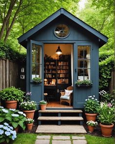 a small blue shed sitting in the middle of a lush green yard with flowers and potted plants