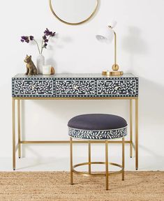 a blue and white desk with a round mirror on the wall above it next to a stool