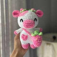 a hand holding a small crocheted cow with flowers on it's tail