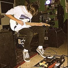 a young man sitting on top of a chair while playing an electric guitar in a room