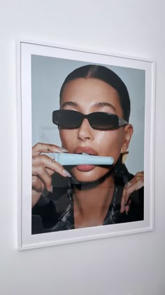 a woman with sunglasses on her face brushing her teeth in front of a white wall