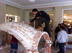 a man standing on top of a brick structure in a room filled with other people