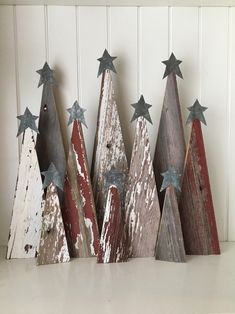 several wooden christmas trees are lined up against a white wall, with stars on them