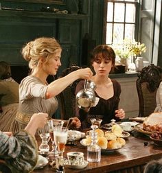 three women sitting at a table with food and drinks in front of them, while one woman pours water from a pitcher