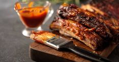 bbq ribs on a cutting board next to a glass of sauce and a knife