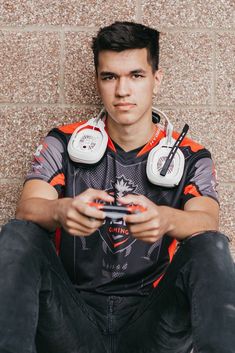 a young man sitting on the ground with headphones around his neck holding a remote control