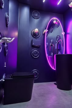 a bathroom with purple lighting and circular mirrors on the wall, along with black trashcans