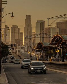 cars are driving down the road in front of tall buildings and skyscrapers at sunset