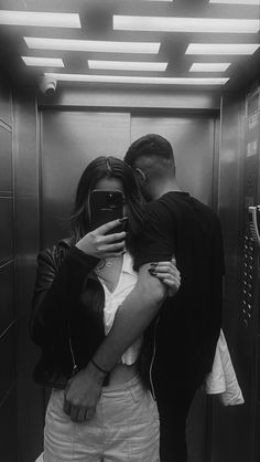 a man and woman standing in front of an elevator taking a selfie with their cell phone