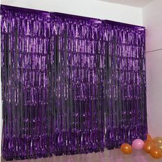 some balloons are sitting on the floor in front of a purple curtain with fringes