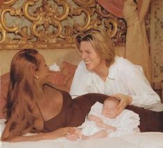 a woman holding a baby while laying on top of a bed