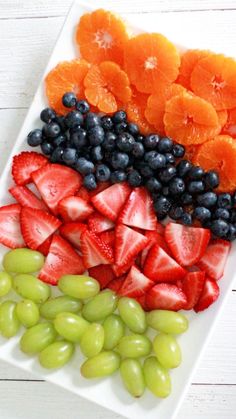 grapes, strawberries, and oranges are arranged on a white platter to look like fruit