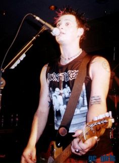 a man holding a guitar while standing in front of a microphone