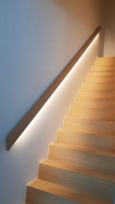 a wooden stair case with lights on the side and below it, along with a white wall