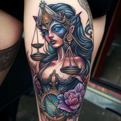 a lady justice tattoo on the leg with scales and flowers around her waist, holding a scale