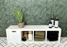 a white shelf with bottles and towels next to a green wallpapered wall behind it