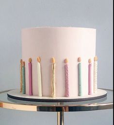 a white cake with pink frosting and colorful candles on the top is sitting on a metal stand