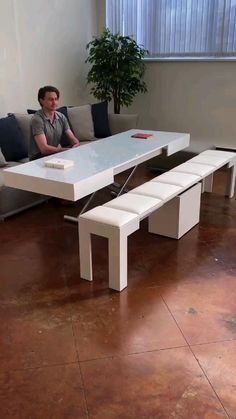 a man sitting on a couch in front of a white table with benches underneath it