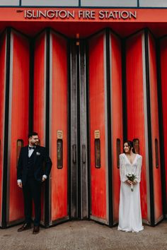 a bride and groom standing in front of red doors at the rington fire station