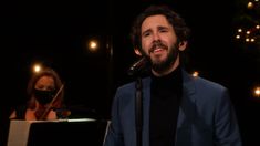 a man in a blue suit singing into a microphone with a woman standing behind him