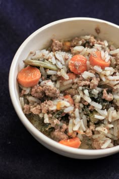 a white bowl filled with rice and meat on top of a blue table cloth next to a fork