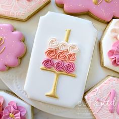 some decorated cookies are on a white plate with pink and gold icing in the shape of a birthday cake