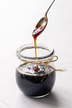 a spoon pouring honey into a jar filled with liquid on top of a white table