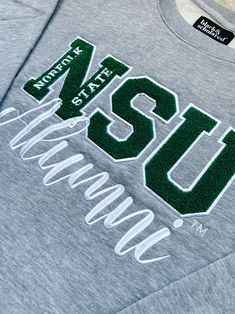 Introducing the Norfolk State™ Alumni Chenille Embroidered Sweatshirt – a timeless piece that celebrates your Spartan pride with elegance and comfort.Emblazoned with the iconic Norfolk State™ emblem, this sweatshirt showcases your enduring connection to your alma mater in exquisite chenille embroidery. It’s not just a garment; it’s a symbol of your academic journey, your achievements, and your unwavering school spirit. Crewneck Sweatshirt:• Features rich, plush chenille embroidery• Rib-knit cuff Athletic Heather Team Spirit Sweatshirt For Streetwear, Collegiate Athletic Heather Sweatshirt For Sports, College Long Sleeve T-shirt With Machine Embroidery, Norfolk State University, Collegiate Team-colored Hooded Sweatshirt, Collegiate Moisture-wicking Sweatshirt For Sports, Chenille Embroidery, Varsity Cardigan, University Apparel