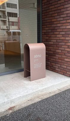 a pink box sitting on the sidewalk in front of a brick building that says abno