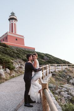 a bride and groom standing on a path in front of a lighthouse