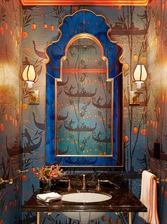 a fancy bathroom with blue and gold walls, an ornate mirror over the sink and two lights on the wall