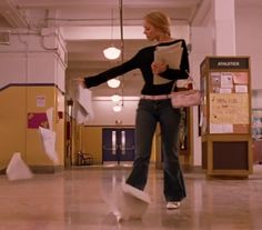 a woman standing in a hallway with her arms spread out and holding a book over her shoulder