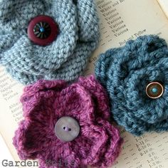 three crocheted flowers sitting on top of an open book next to a button