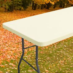 a white table sitting on top of a lush green field next to trees covered in fall leaves