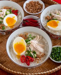 four bowls filled with rice, meat and eggs on top of a wooden tray next to red peppers