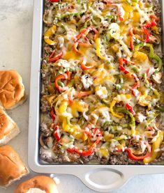 a casserole dish with cheese, peppers and other toppings next to rolls