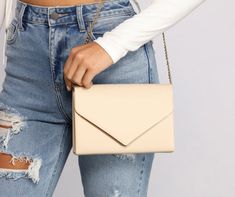 a woman in ripped jeans holding a white purse with an envelope on the front pocket