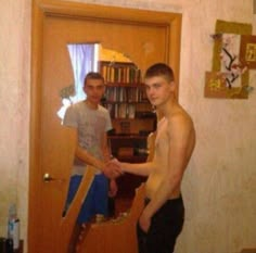 two young men standing in front of a door with no shirt on and one holding his hand out to the other