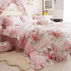 a bed with pink and white flowers on the comforter, pillows and rugs