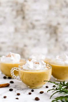 three cups filled with whipped cream on top of a white table next to cinnamon sticks