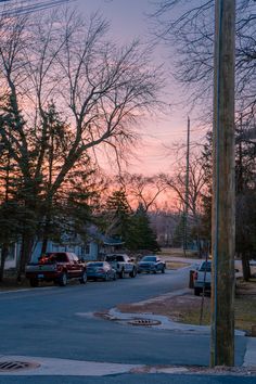 cars are parked on the street in front of some houses at sunset or sunrise time